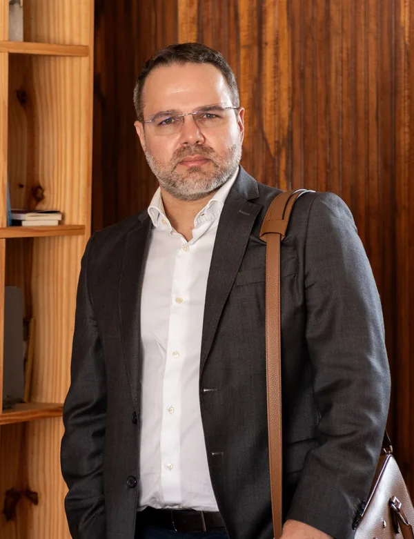 Dr. Geraldo Capuchinho, cirurgião plástico em Belo Horizonte, de paletó escuro e camisa branca, em pé no consultório